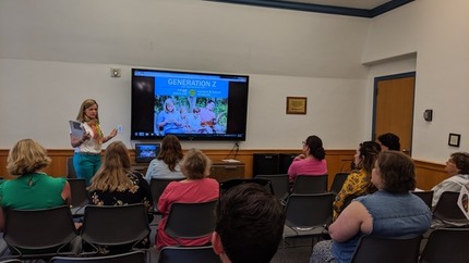 Presenter pointing to screen and talking to small audience of people.