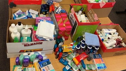 A table filled with boxes and bags overflowing with hygiene products like toothbrushes, deodorant, soap, and feminine hygiene products.