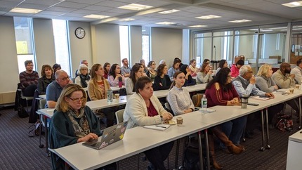 Large group of people sitting in chairs at tables waiting for a presentation.