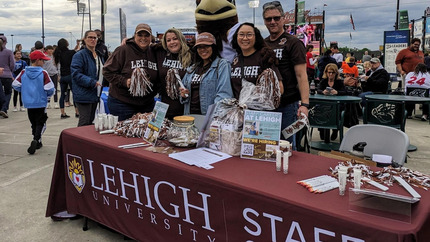 Group of people standing around an information table with brown, Lehigh table cloth.